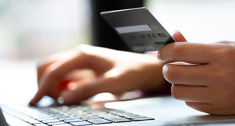 A person holds their credit card as they type their information into a laptop.