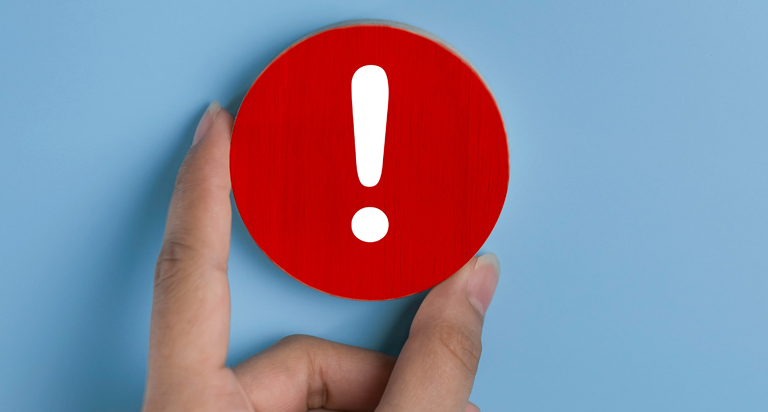 A woman’s hand positions a red disc with a white exclamation point on the front as it rests on a light blue background.